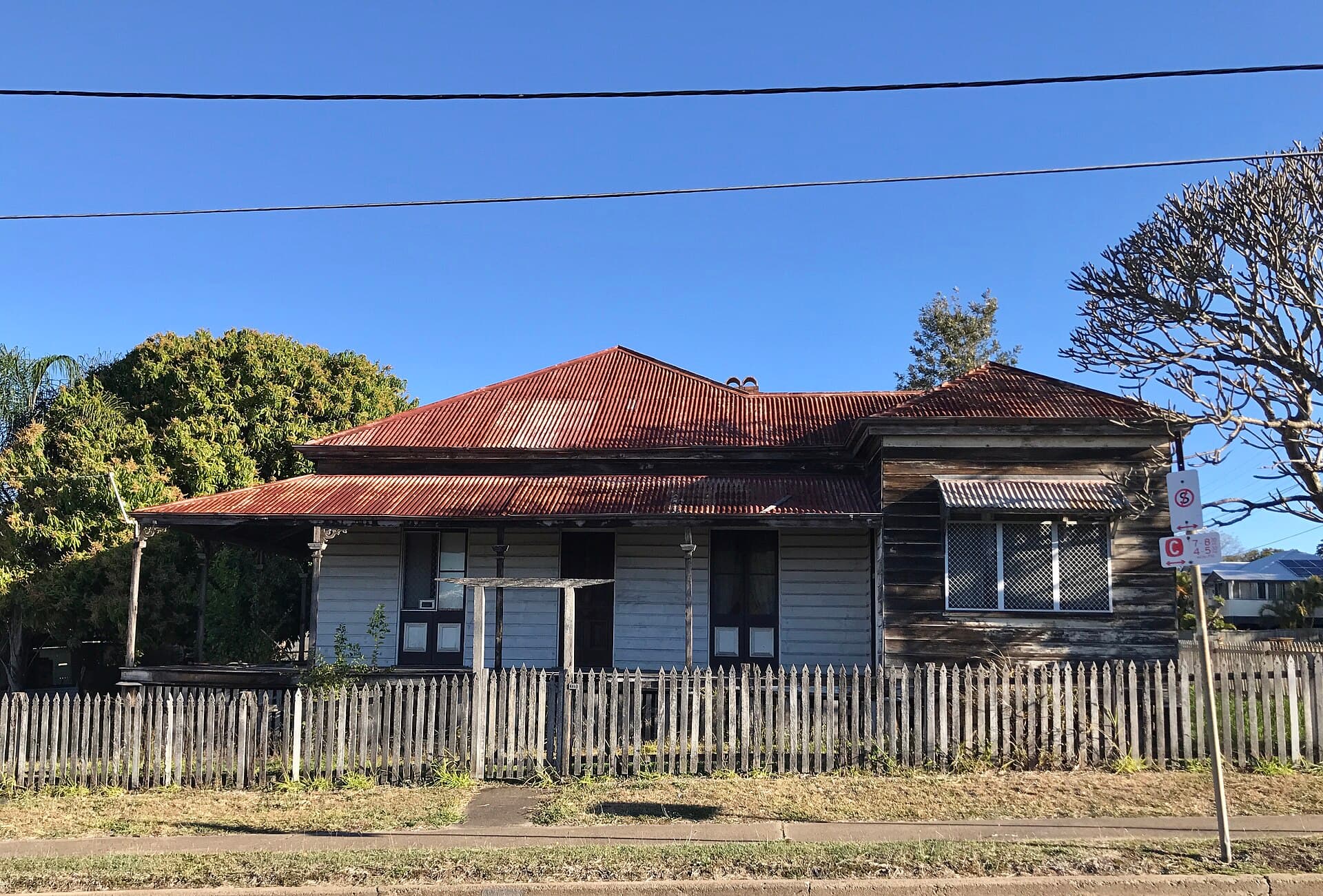 A high-set Queenslander with a tiled roof in afternoon light, the sort of house whose restoration is never as simple as a flyer suggests